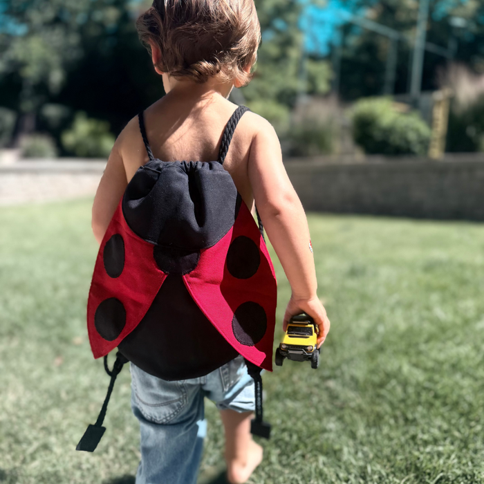 Small children's drawstring backpack with red ladybug wing flaps.