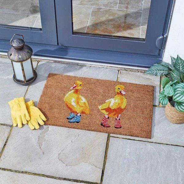 Rectangular coir doormat printed with a row of ducks wearing wellington boots, shown flat from above