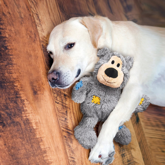 Yellow Labrador lying on a wooden floor with a grey KONG Wild Knots plush bear held between its front paws
