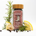 Jar of dark pink salt with wooden lid. Rosemary sprigs, peppercorns, and lemon wedges placed around jar.