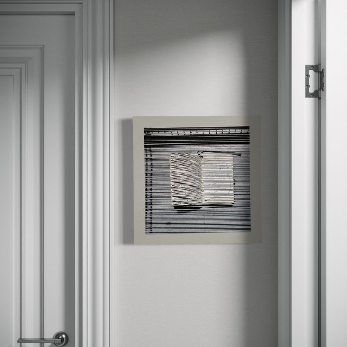 The artwork 'Sentence Structure String 1' by Anne Sherwood Pundyk features a monochromatic square composition with layered horizontal lines and a central stack of folded or rippled forms. The black and white archival inkjet print mounted on wood panel creates a striking contrast against the light wall, emphasizing geometric patterns and textural elements. By Anne Sherwood Pundyk.